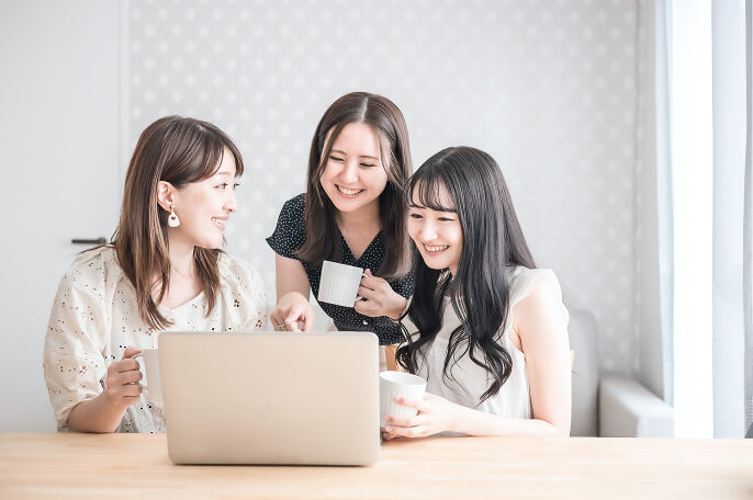 ノートパソコンの前に集まっている笑顔の3人の女性