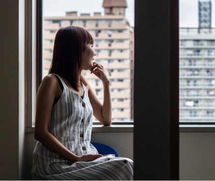窓枠に肘をかけて外を見ている女性
